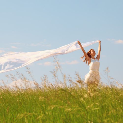The young beautiful girl in a white dress enjoys a wind, the sun
